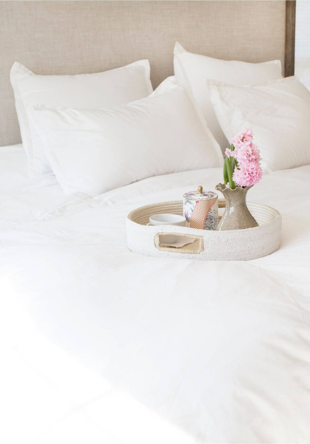 White bed with pillows and a tray holding a teapot and flowers.