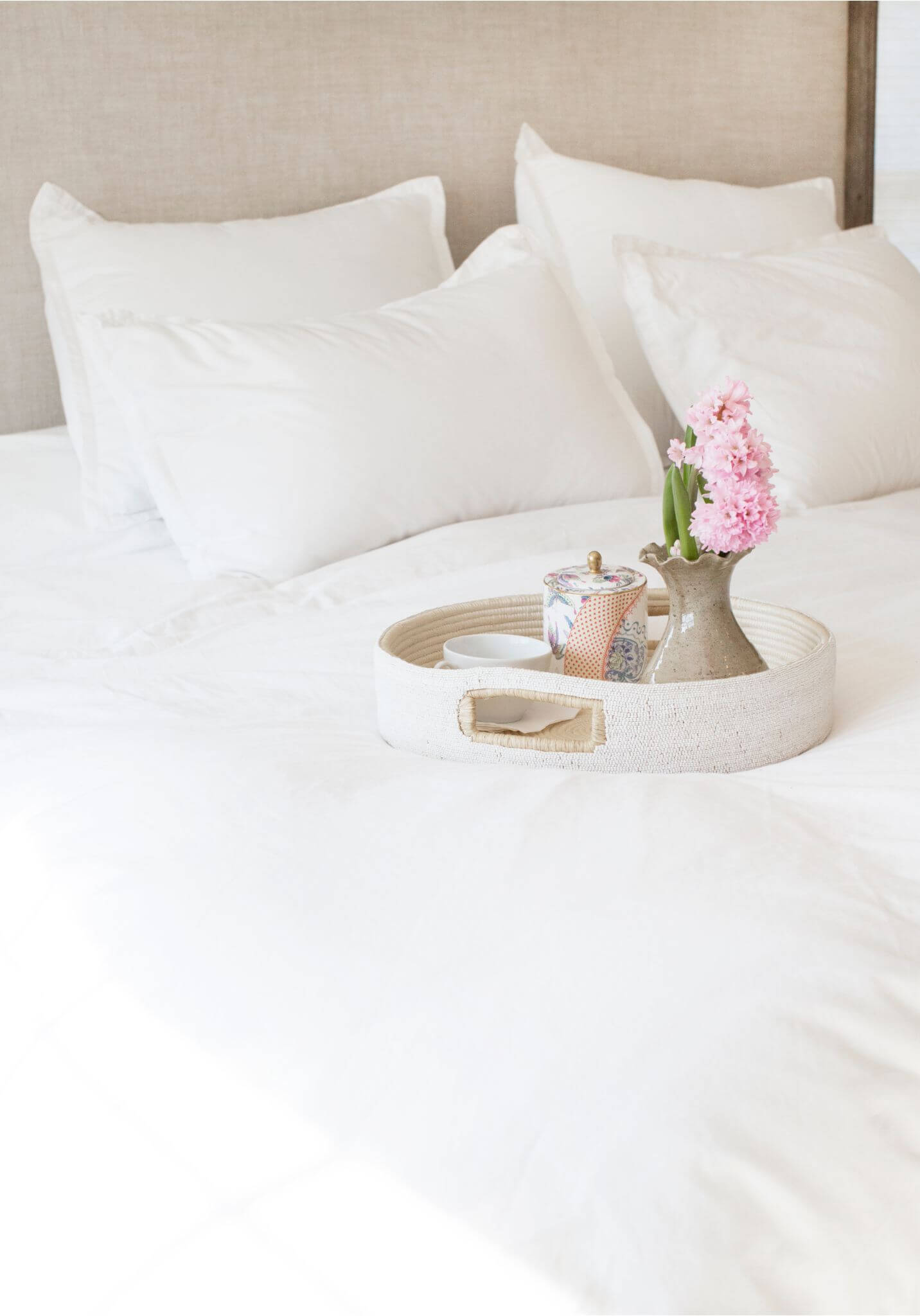 White bed with pillows and a tray holding a teapot and flowers.