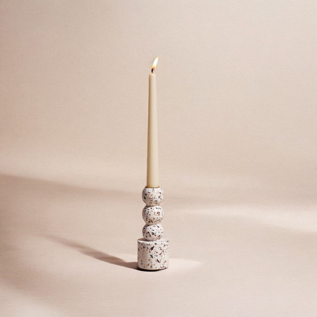 Ceramic candle holder with a lit candle on a beige background