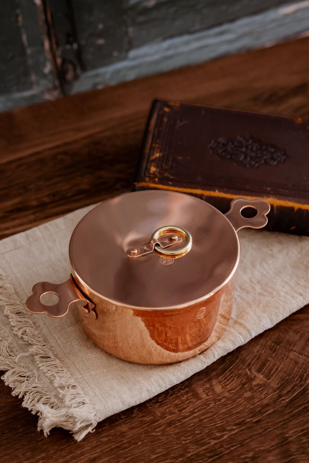 Copper pot on a wooden surface with a leather book in the background