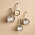 Set of four metallic measuring spoons on a beige background