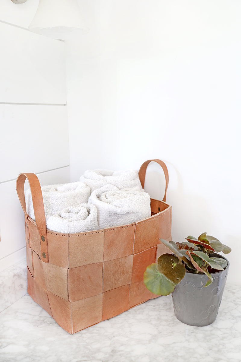 Brown woven basket with white towels on a white surface
