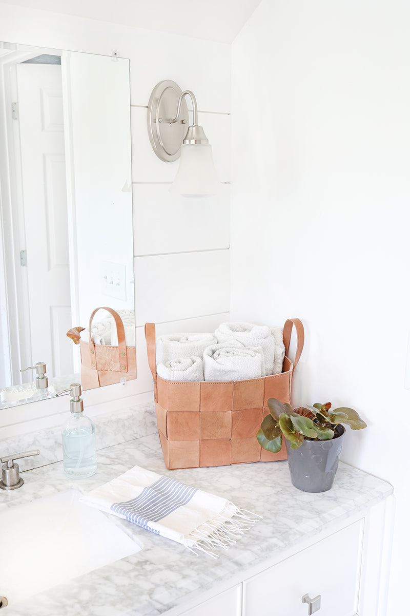 Bathroom counter with woven baskets, towels, and a plant on a white tiled wall background
