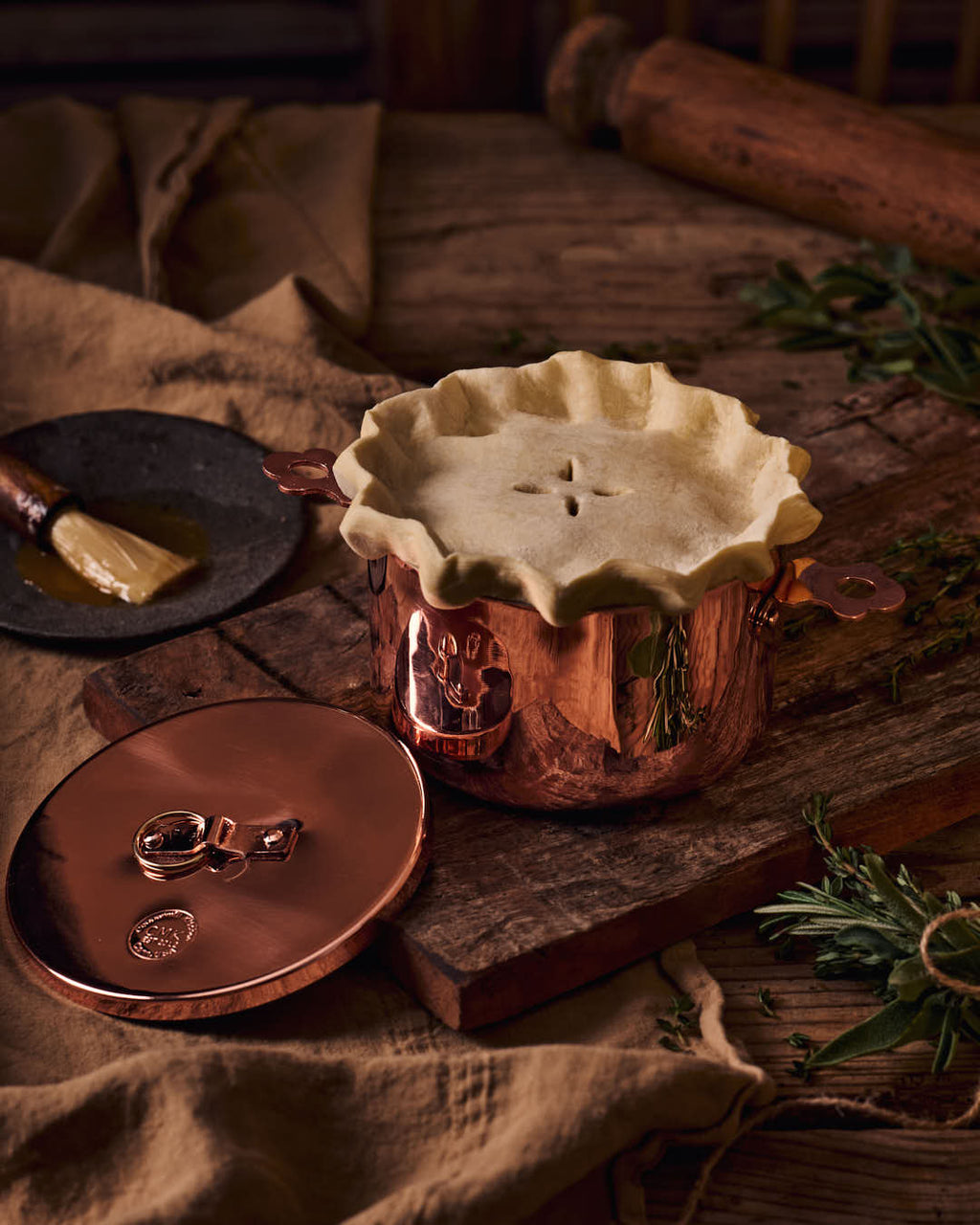 Copper pot with a pie on top, surrounded by rustic kitchen items on a wooden surface.