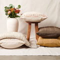 Decorative pillows and a small stool with a vase of flowers on a light background