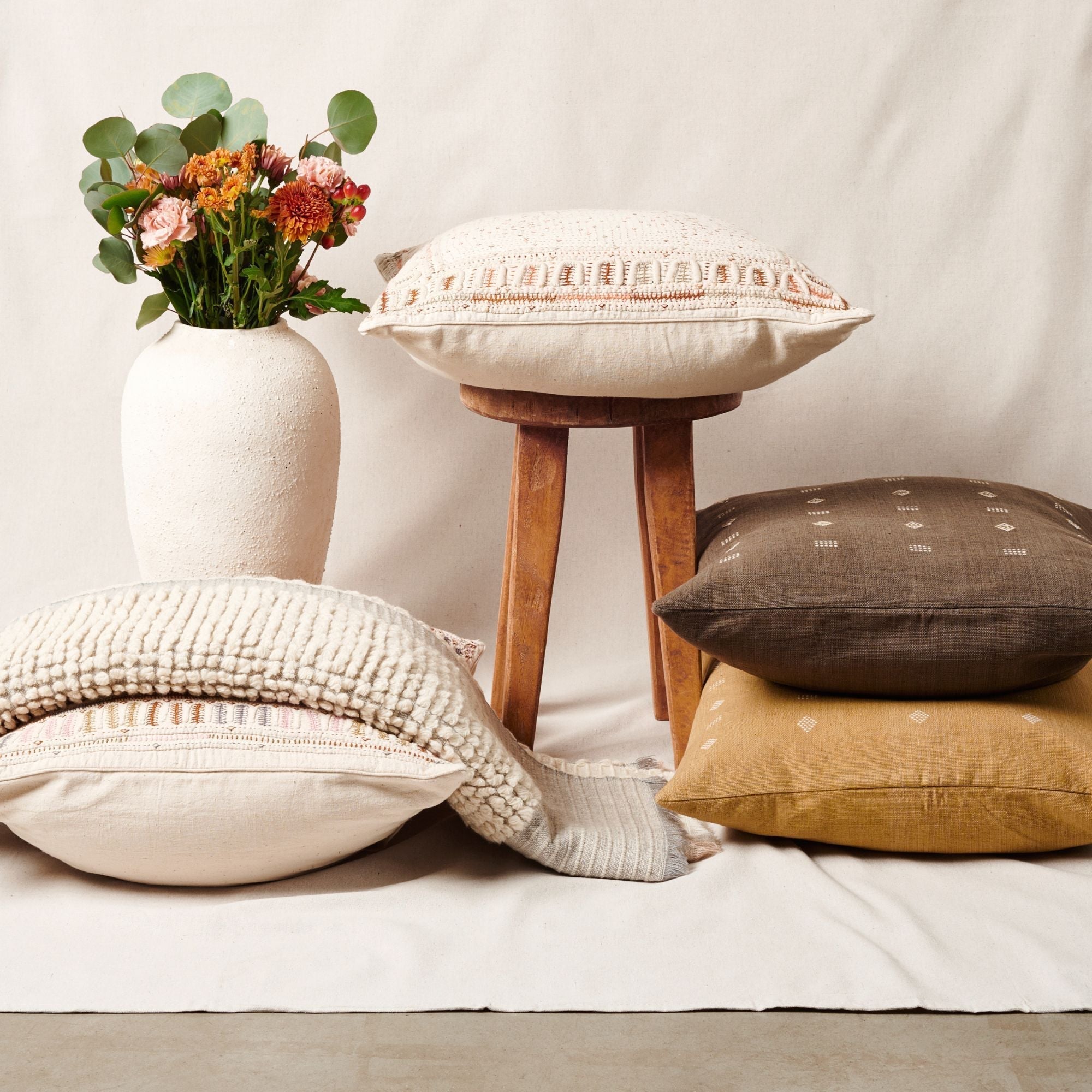 Decorative pillows and a small stool with a vase of flowers on a light background