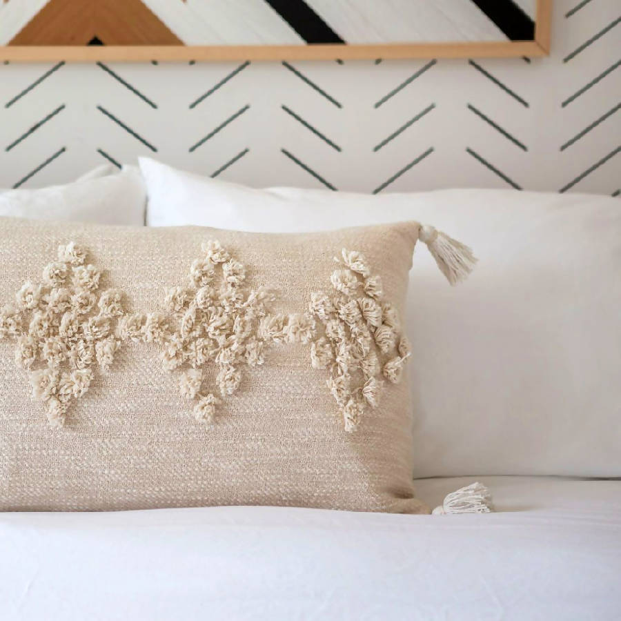 Decorative pillow with floral patterns on a bed against a geometric wall design.