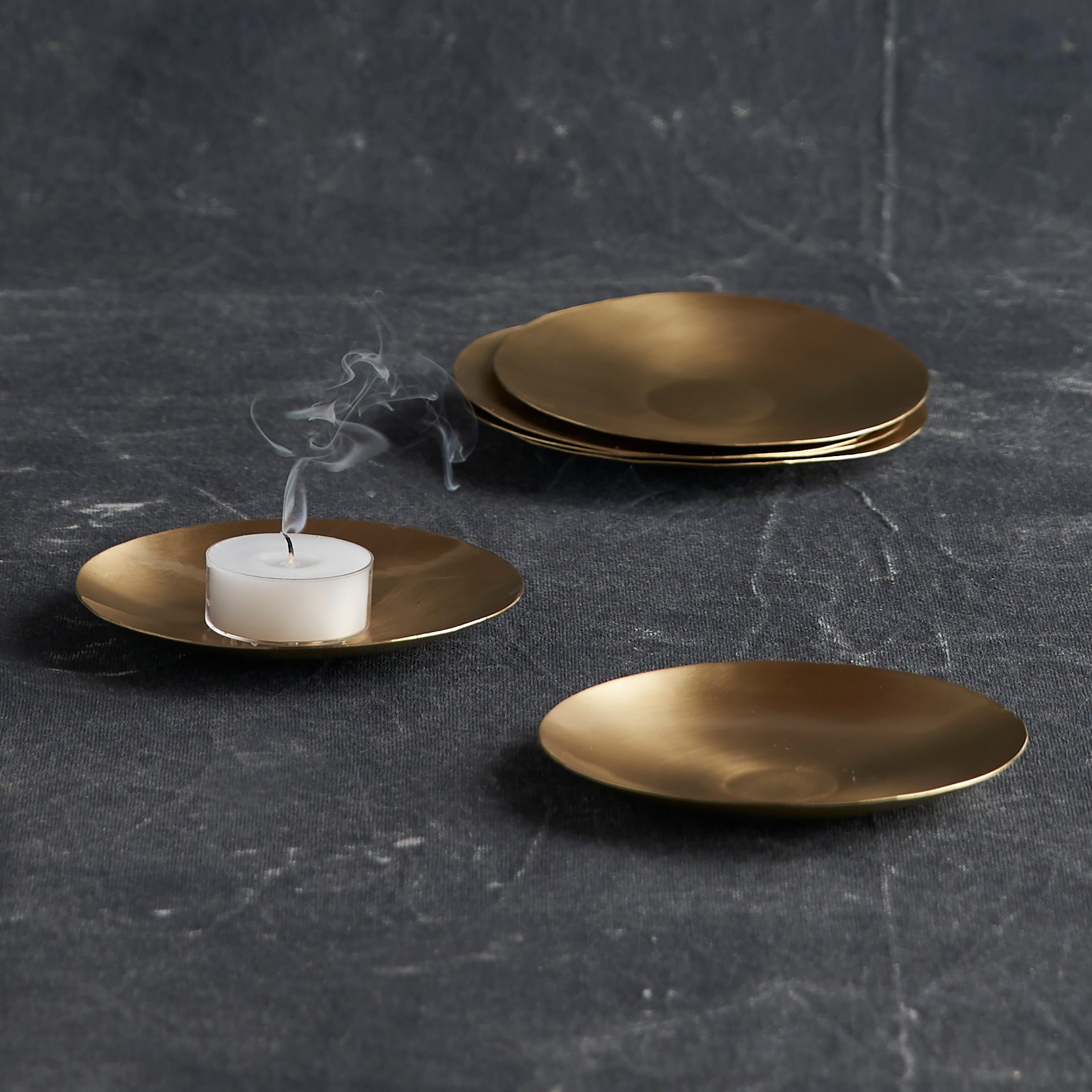 Gold plates with a white candle on a dark textured surface