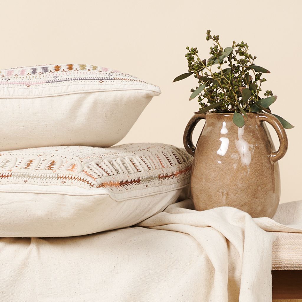 Decorative pillows and a vase with greenery on a neutral background
