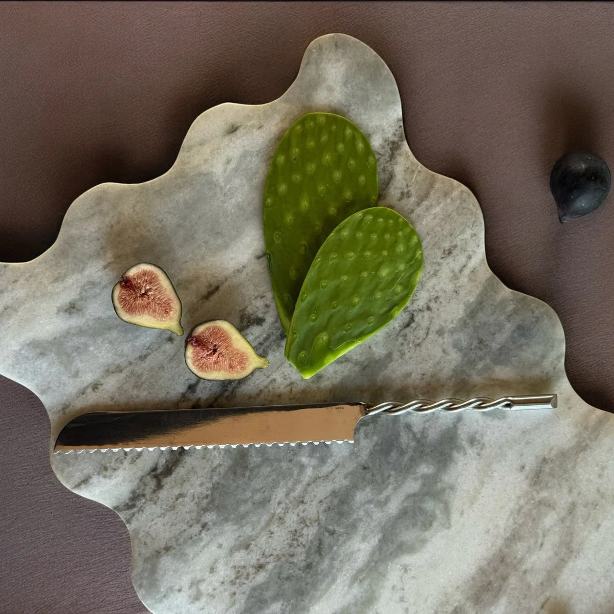 Marble cutting board with figs, a cactus leaf, and a knife on a brown background