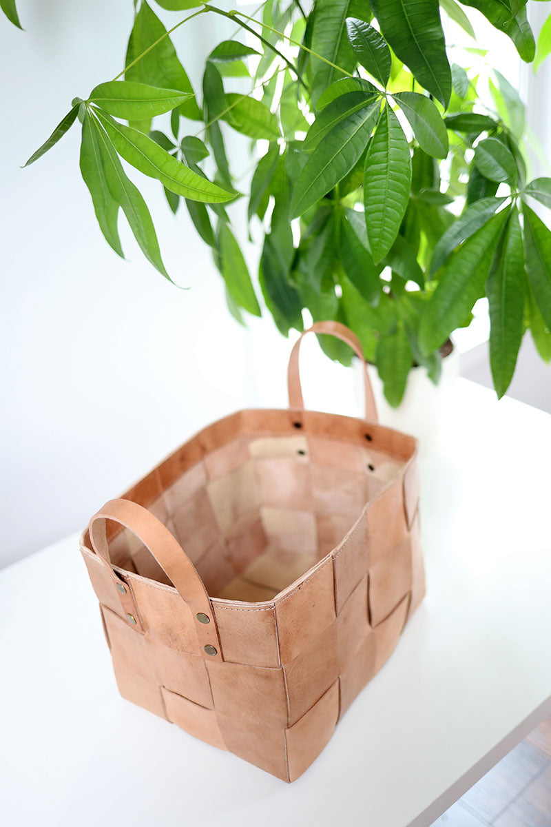 Brown woven basket on a white surface with green leaves in the background