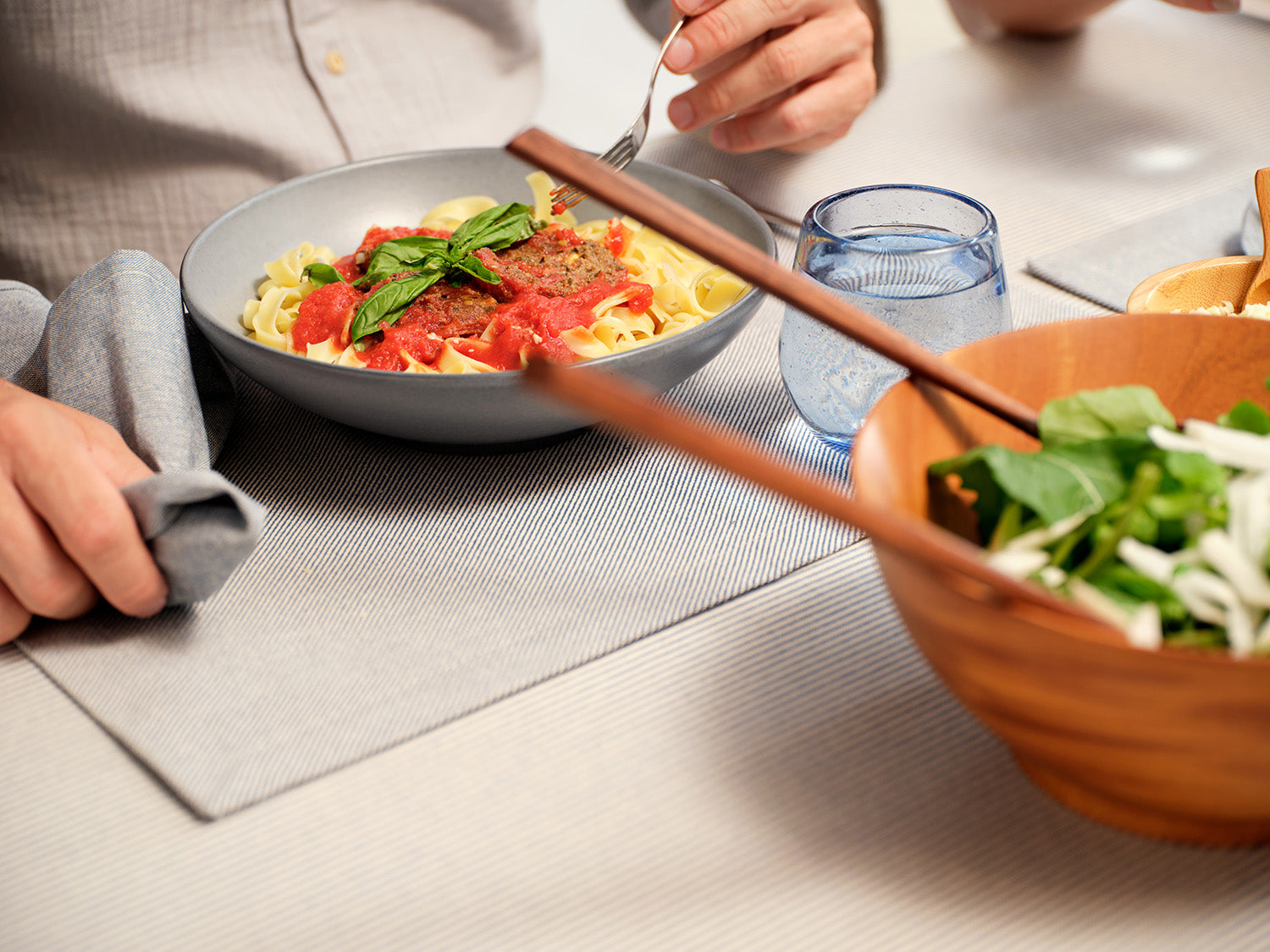 Person eating pasta with a side salad at a table. Cloth napkin/placemat