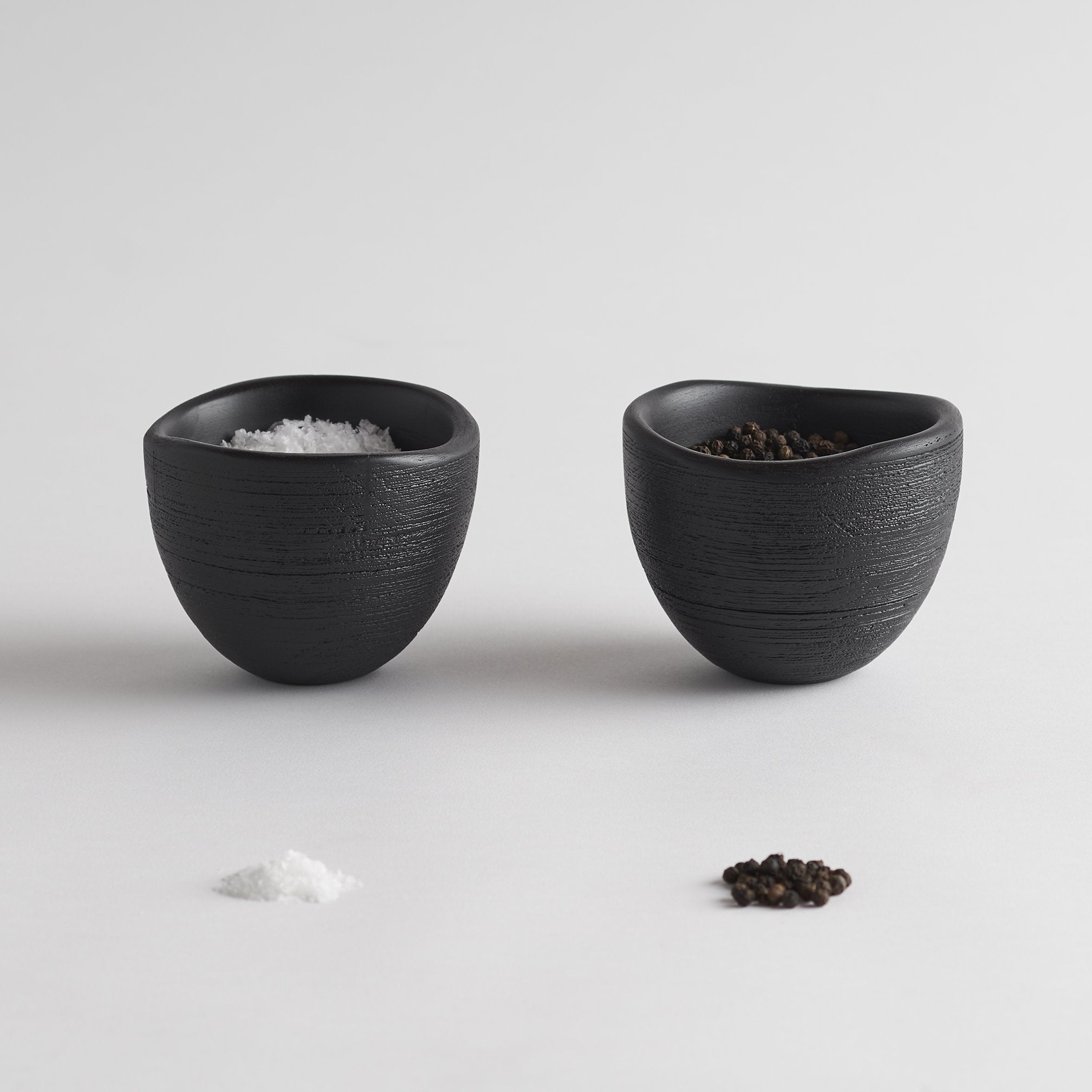 Two black ceramic bowls with salt and pepper on a light gray background