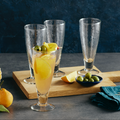 Mimosa in a Pebbled Flute with olives and lemon slices in a glass on a wooden board with a dark background