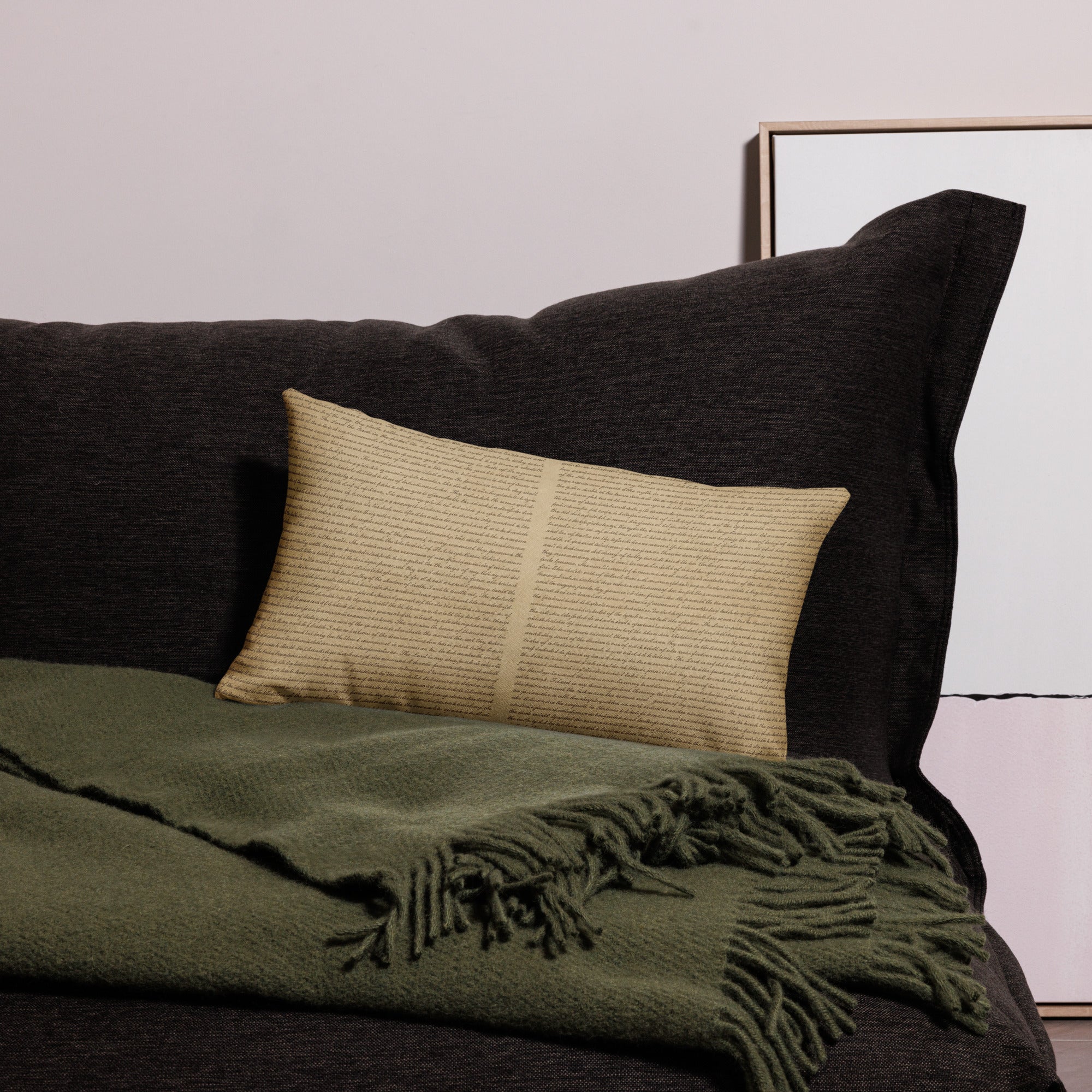 Soft beige Luxury Comfort Pillow resting on a dark charcoal sofa with an olive green fringed throw, showcasing a cozy and elegant home decor setting.