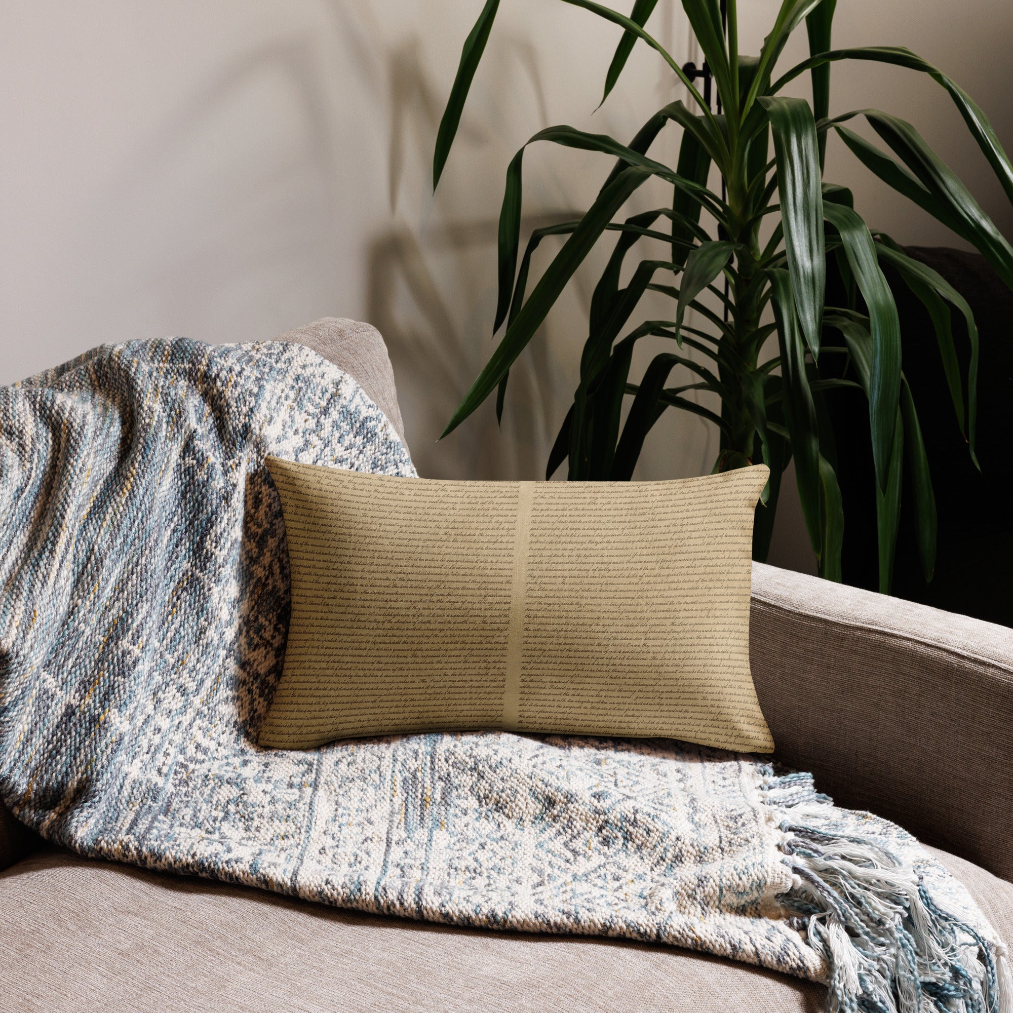 Luxury Comfort Pillow resting on a beige sofa with a textured blue and white woven throw, accompanied by a green houseplant in the background, creating a cozy interior setting.
