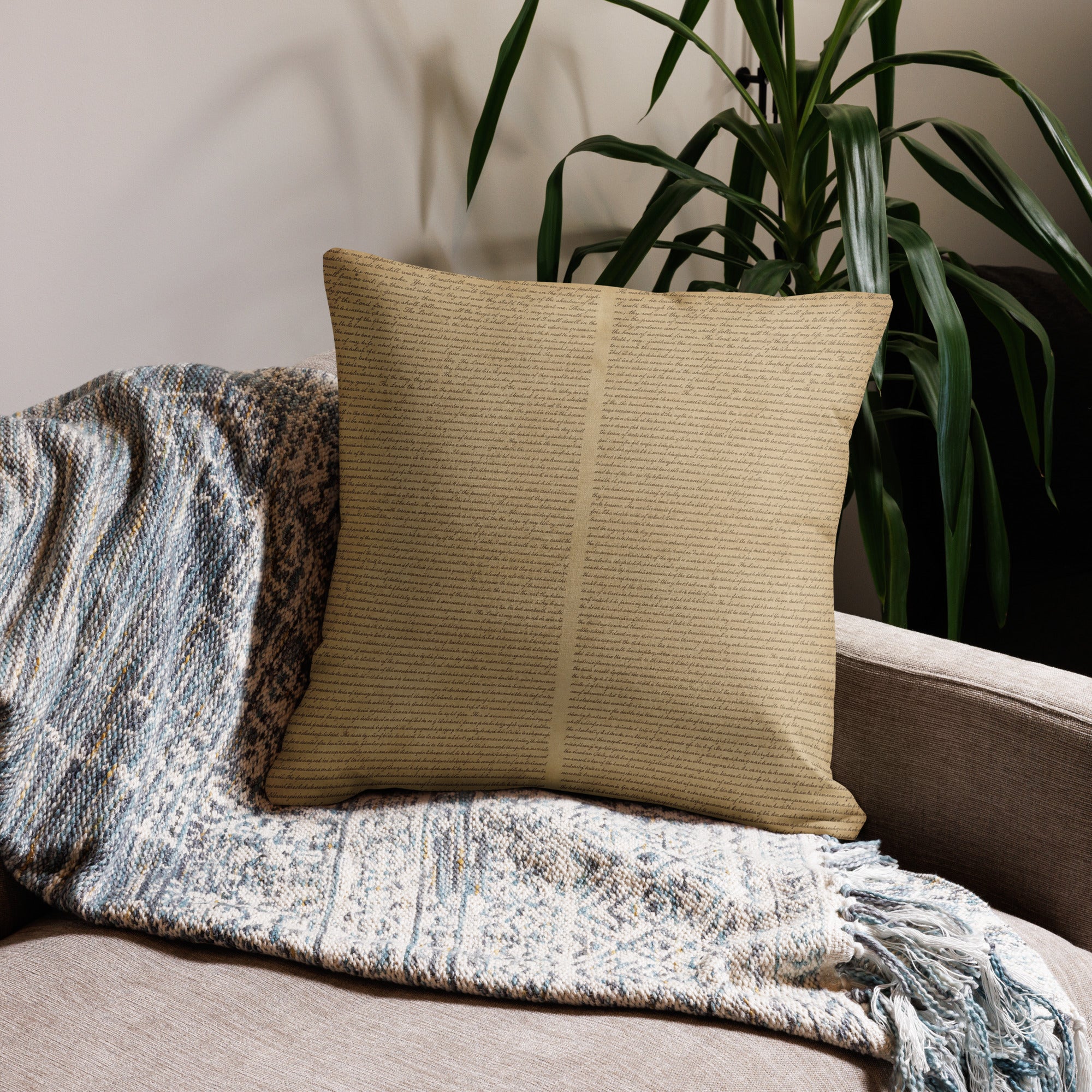 Luxury Comfort Pillow with a subtle text pattern placed on a cozy textured throw blanket on a sofa, next to a green leafy plant in a stylish living room setting.