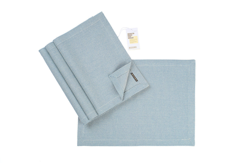 Light blue textured napkin/placemat set with a folded towel and a tag on a white background