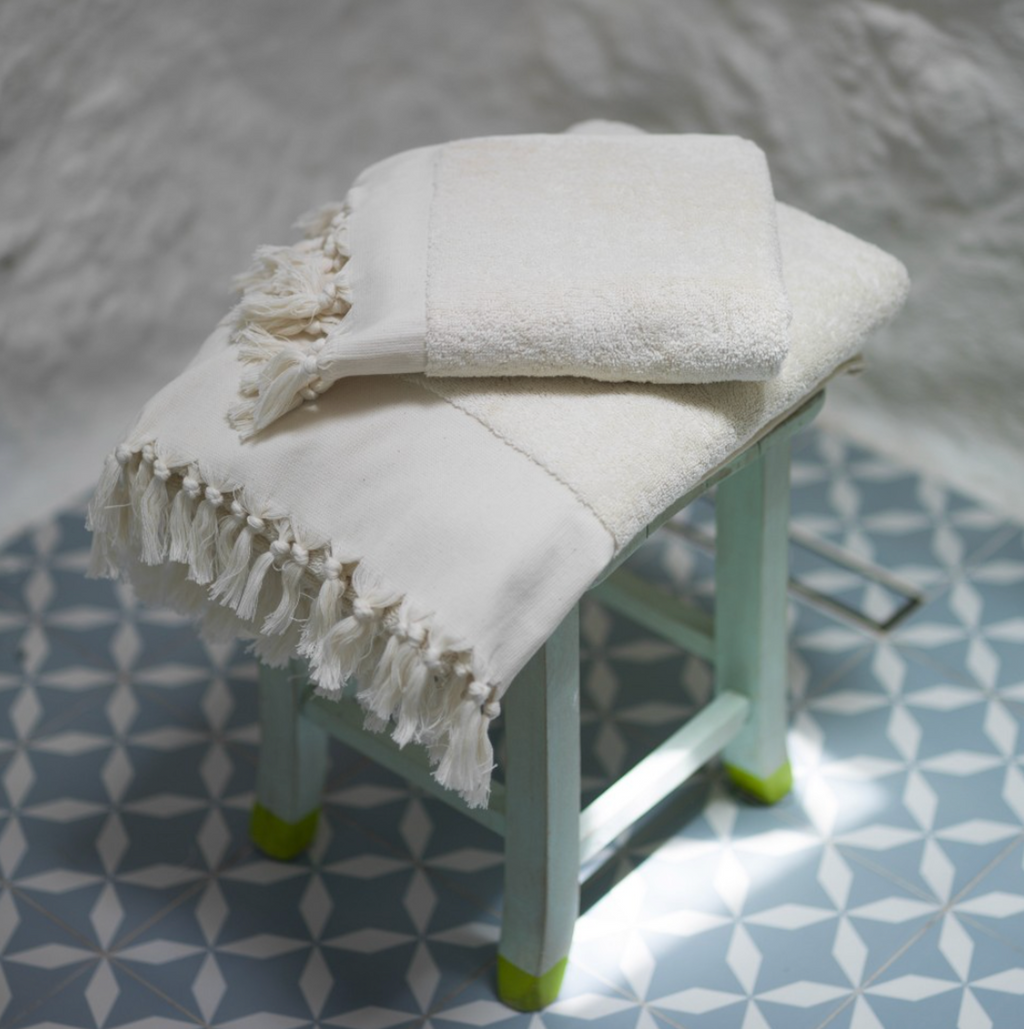 White towel with fringes draped over a small stool on a patterned floor.