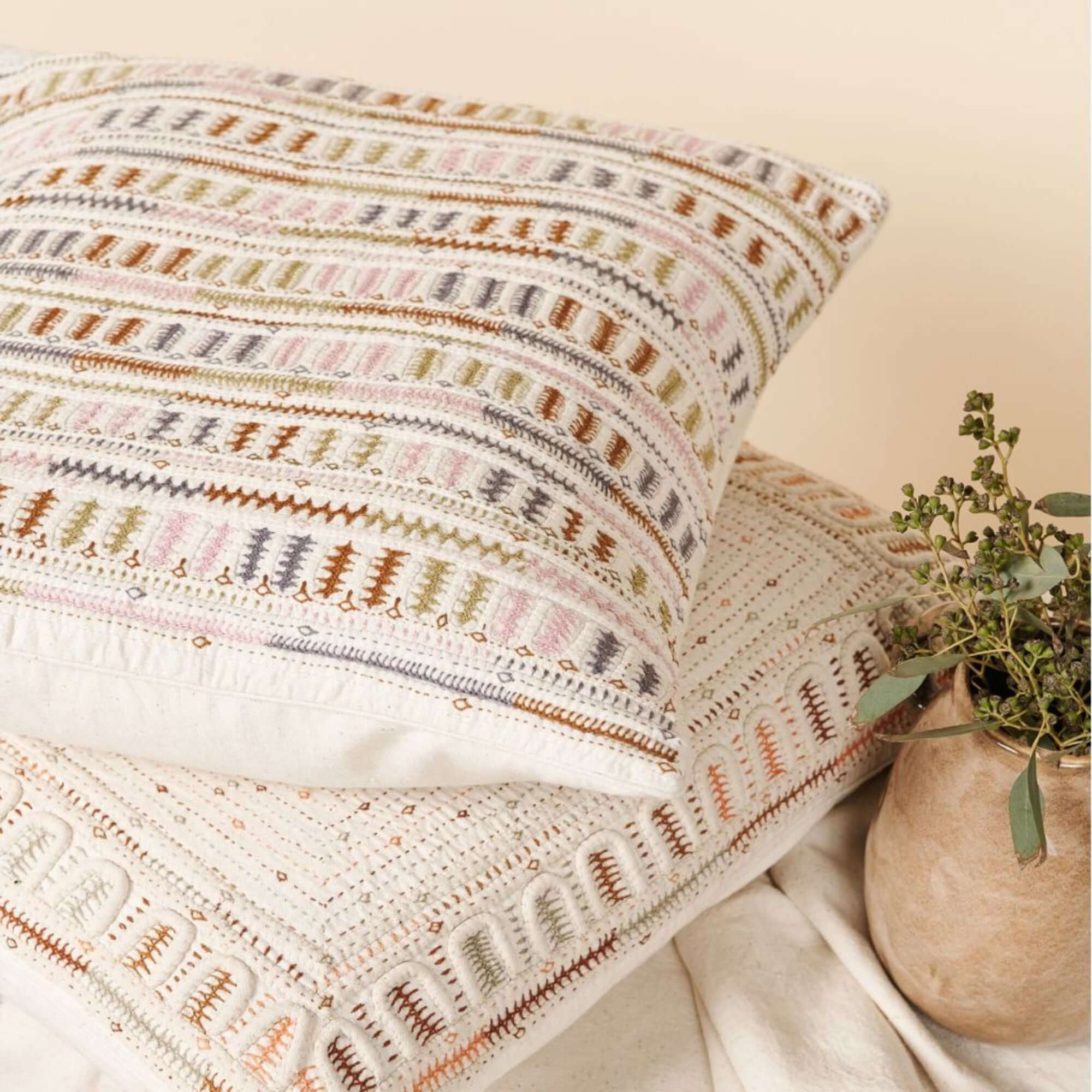 Textured pillows with patterned pillow and plant on a neutral background