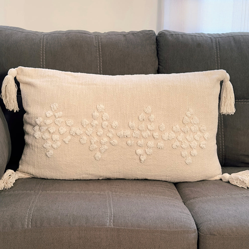 Beige pillow with tassels on a gray sofa