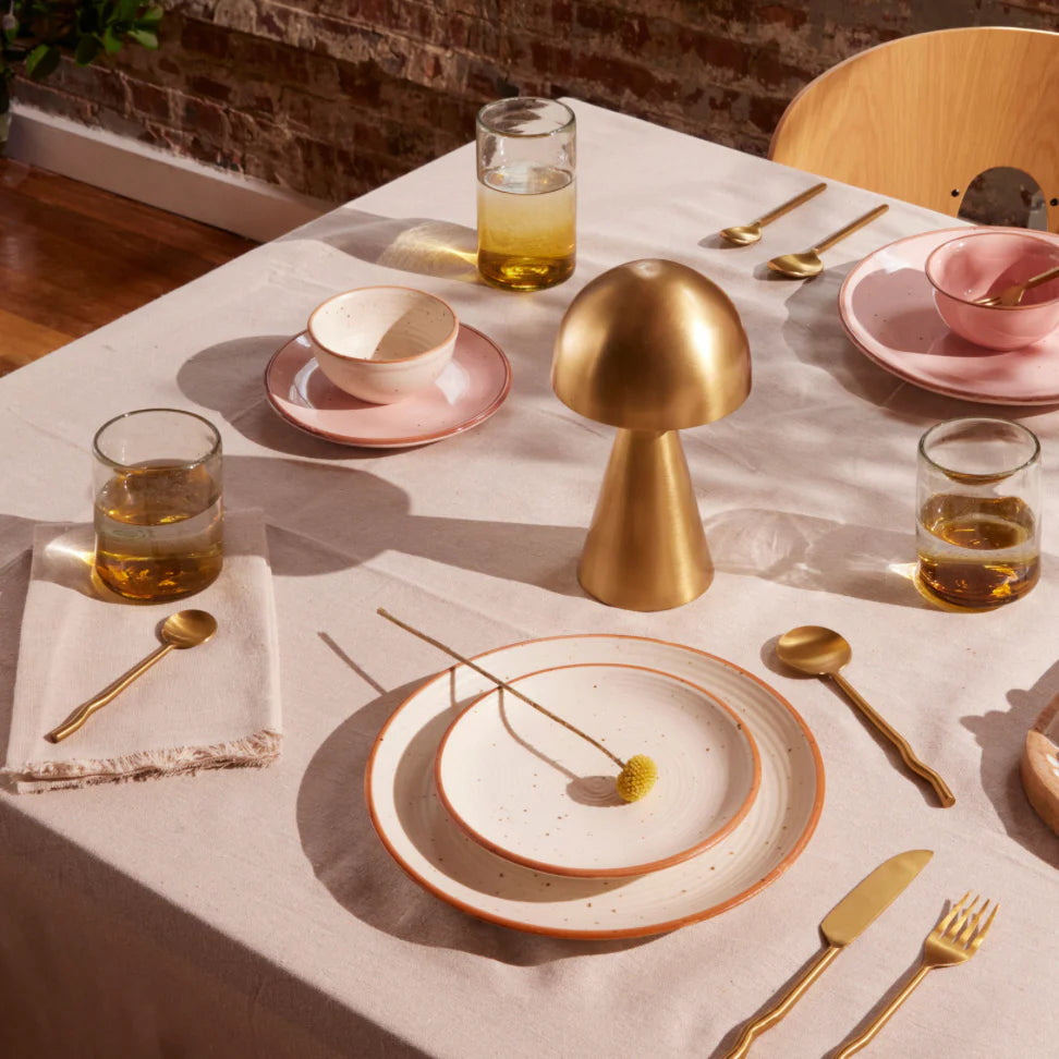 Dining table setting with gold clear gold glasses and pink tableware, including a gold mushroom-shaped center piece.