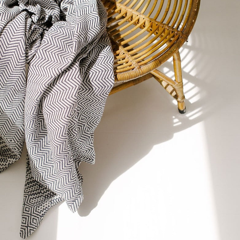 Black and white patterned blanket draped over a wicker chair on a light wooden floor.