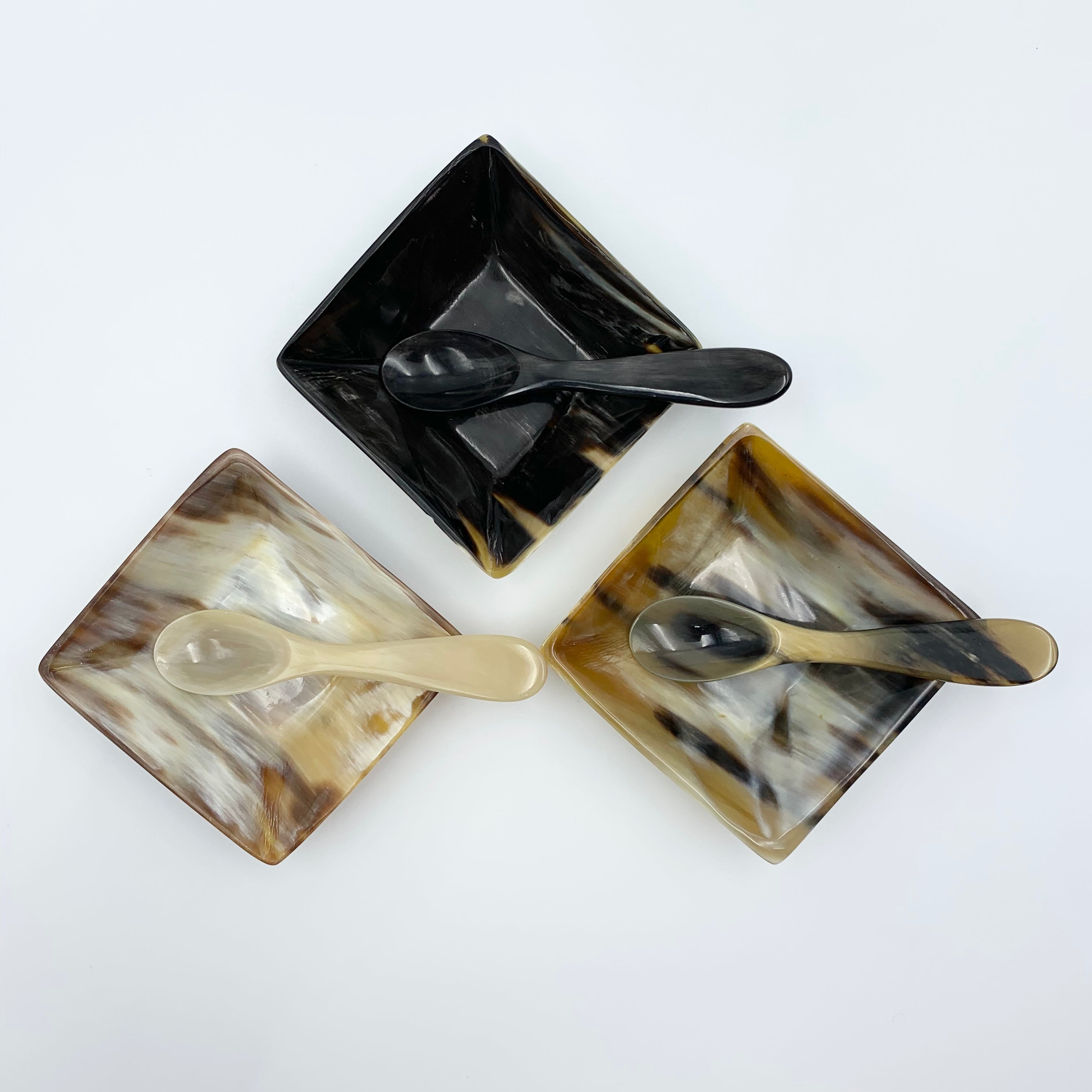 Three square ceramic dishes with spoons on a white background