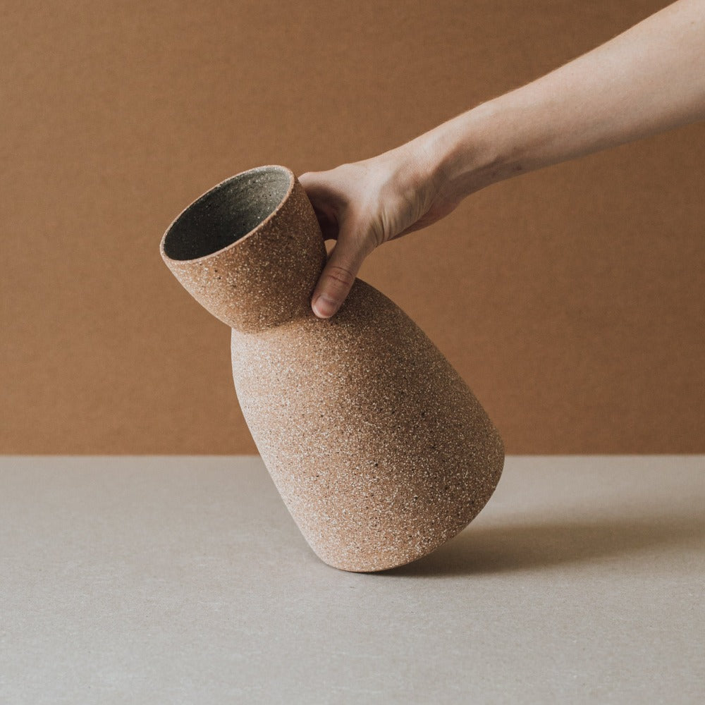 Hand holding a textured ceramic vase against a brown background