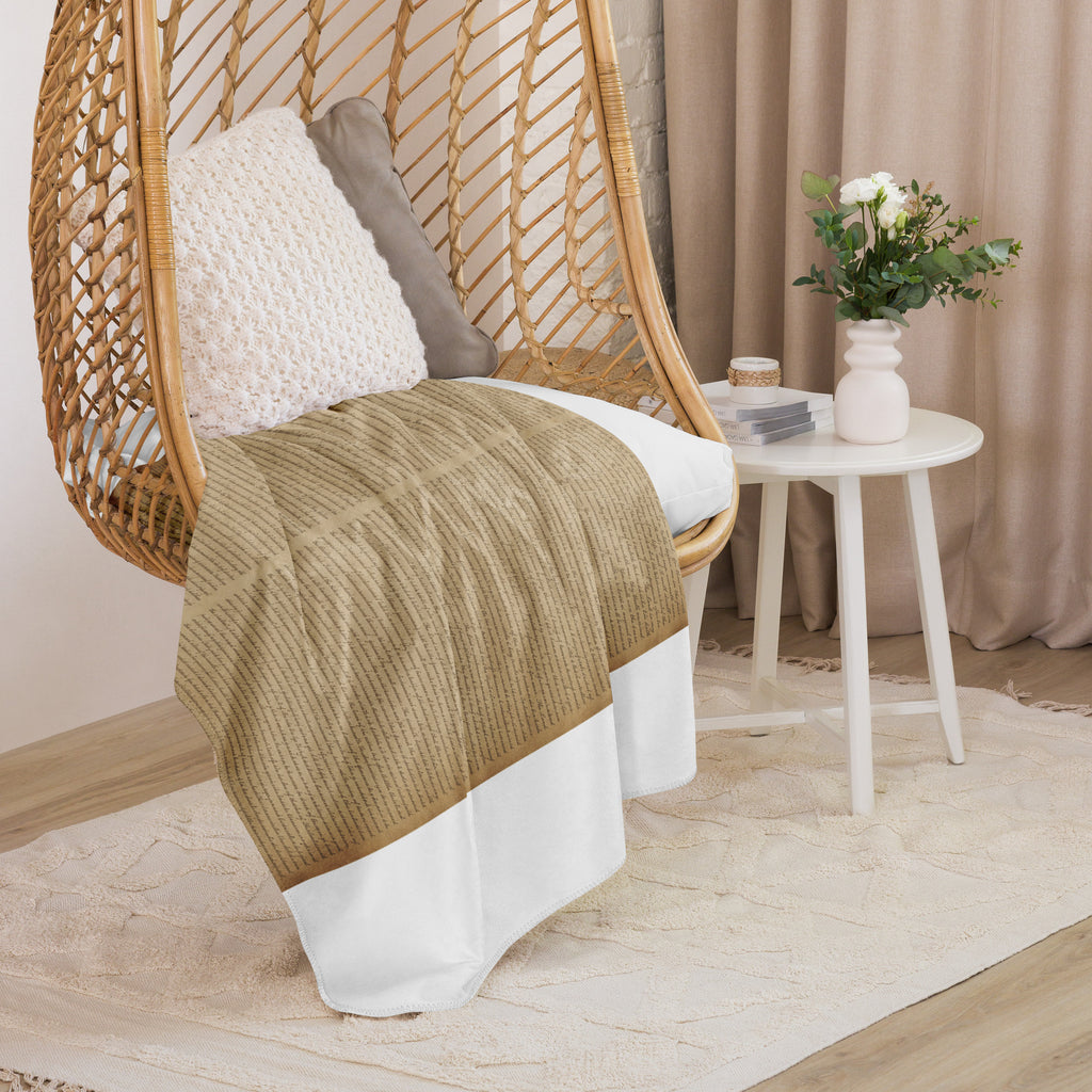 Luxury Sherpa Throw Blanket — Signature Edition in soft tan draped over a wicker chair with neutral pillows beside a white side table with a vase of fresh flowers in an elegant living space