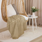 Luxury Sherpa Throw Blanket draped over a woven hanging chair with white cushion, next to a white side table holding a small vase of flowers and decorative items in a cozy room setting.