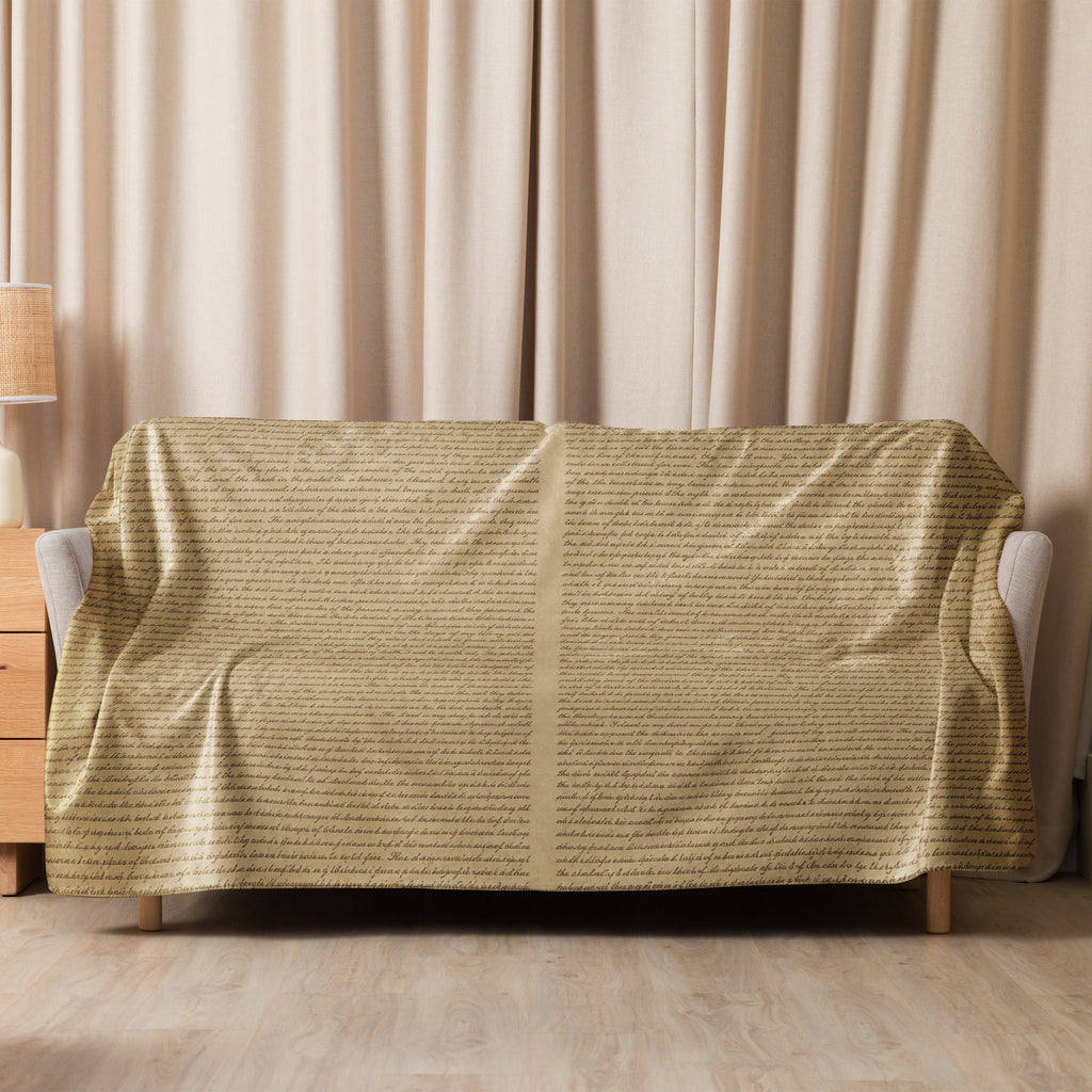 Luxury Sherpa Throw Blanket draped over a sofa in a cozy living room setting, featuring a soft tan color and subtle text pattern, complementing elegant home decor.